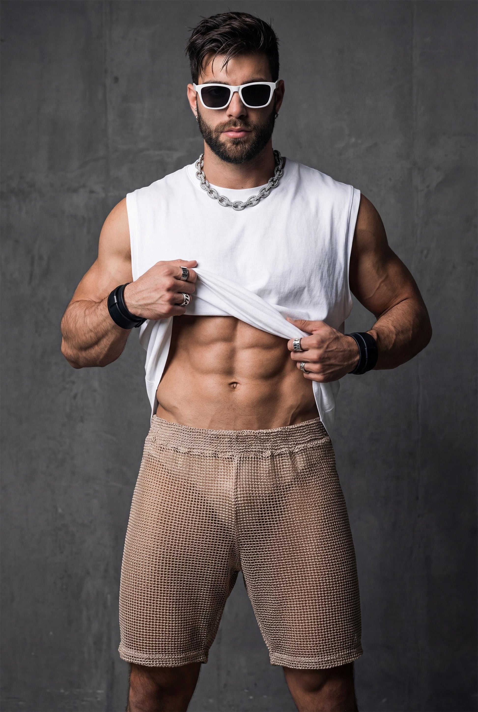 Front view of beige transparent mesh shorts worn by a muscular man. Sheer fabric reveals the body underneath while keeping a fitted, athletic cut. Designed for gay club wear, Berlin nightlife, circuit parties, and pride events. Sexy, breathable party shorts for men who want bold, confident, and eye-catching club outfits.