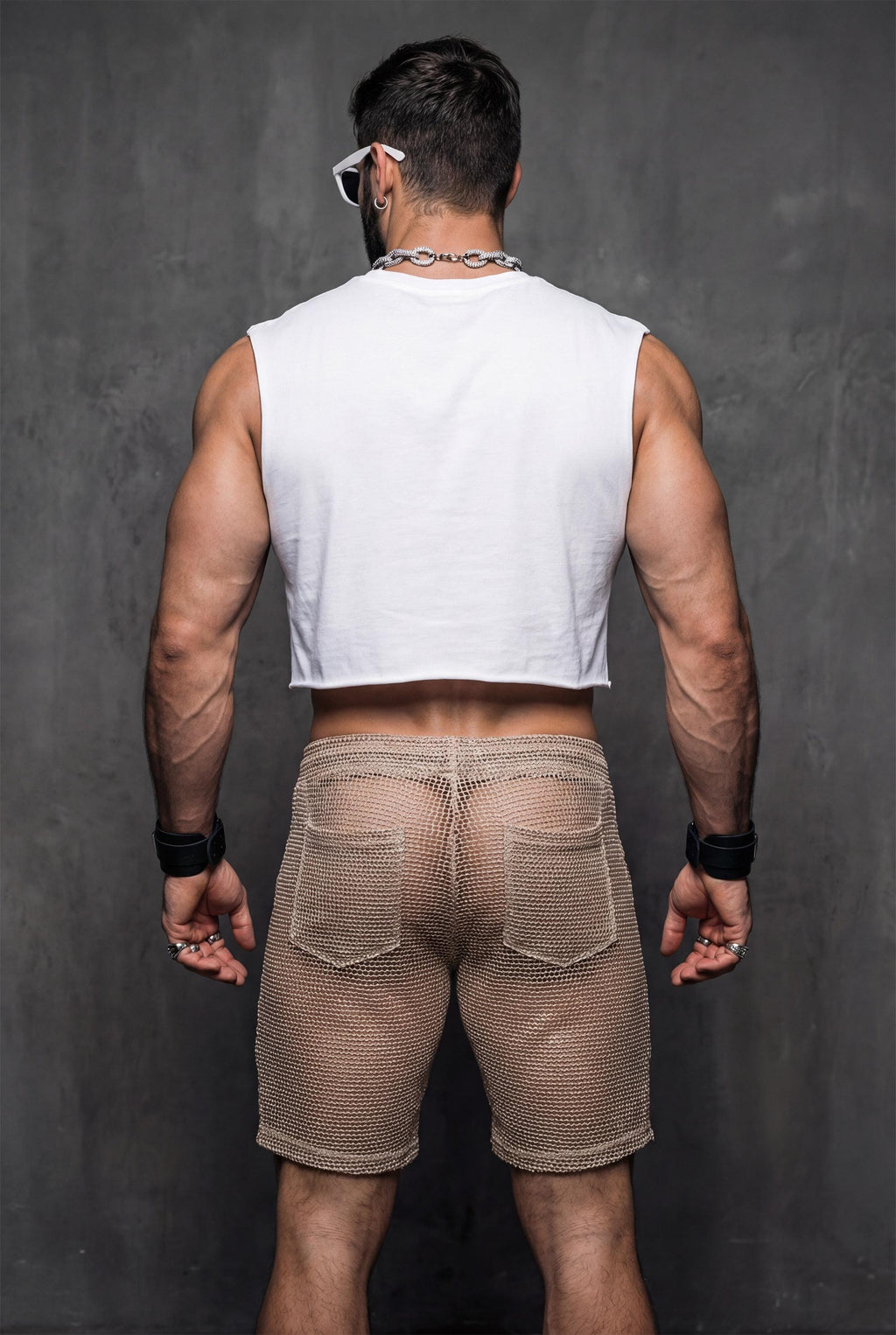 Back view of transparent black mesh shorts on a muscular man. Sheer fabric emphasizes curves and leg definition. Perfect for gay club wear, Berlin party scene, circuit events, and fetish-inspired nightlife. Bold mesh shorts for men seeking sexy, provocative, and breathable party clothing with strong visual impact.