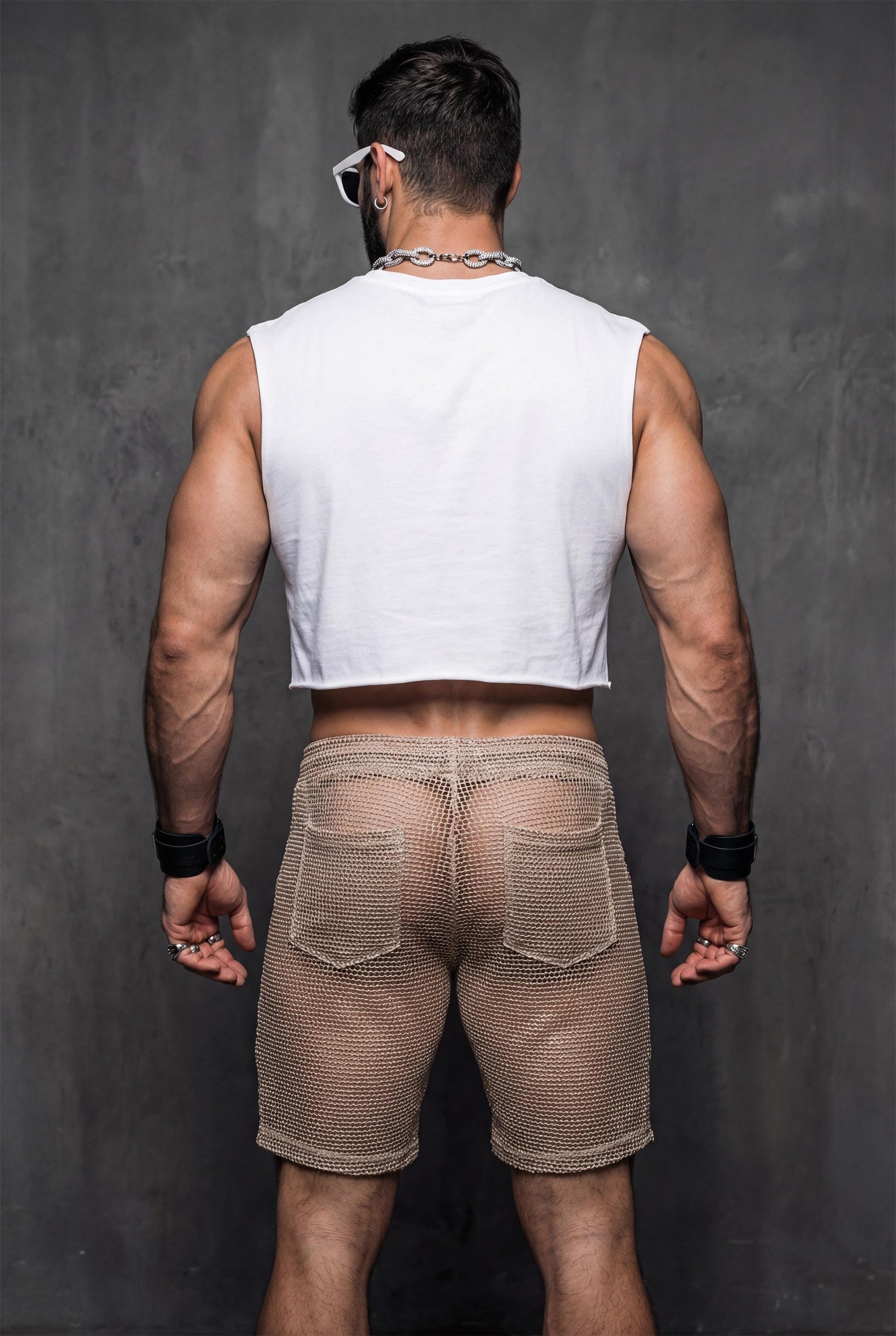 Back view of transparent black mesh shorts on a muscular man. Sheer fabric emphasizes curves and leg definition. Perfect for gay club wear, Berlin party scene, circuit events, and fetish-inspired nightlife. Bold mesh shorts for men seeking sexy, provocative, and breathable party clothing with strong visual impact.