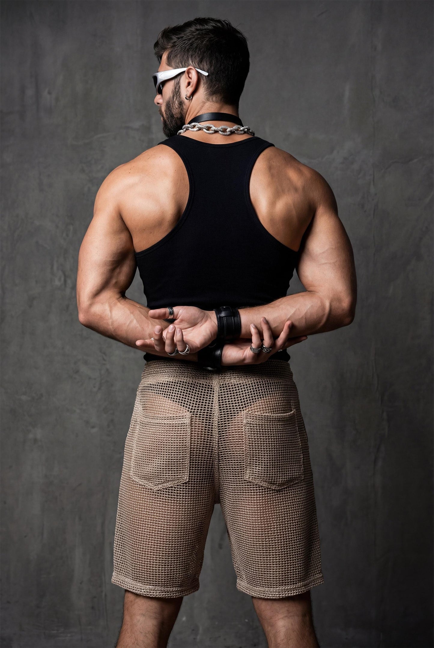 Back view of transparent black mesh shorts on a muscular man. Sheer fabric emphasizes curves and leg definition. Perfect for gay club wear, Berlin party scene, circuit events, and fetish-inspired nightlife. Bold mesh shorts for men seeking sexy, provocative, and breathable party clothing with strong visual impact.