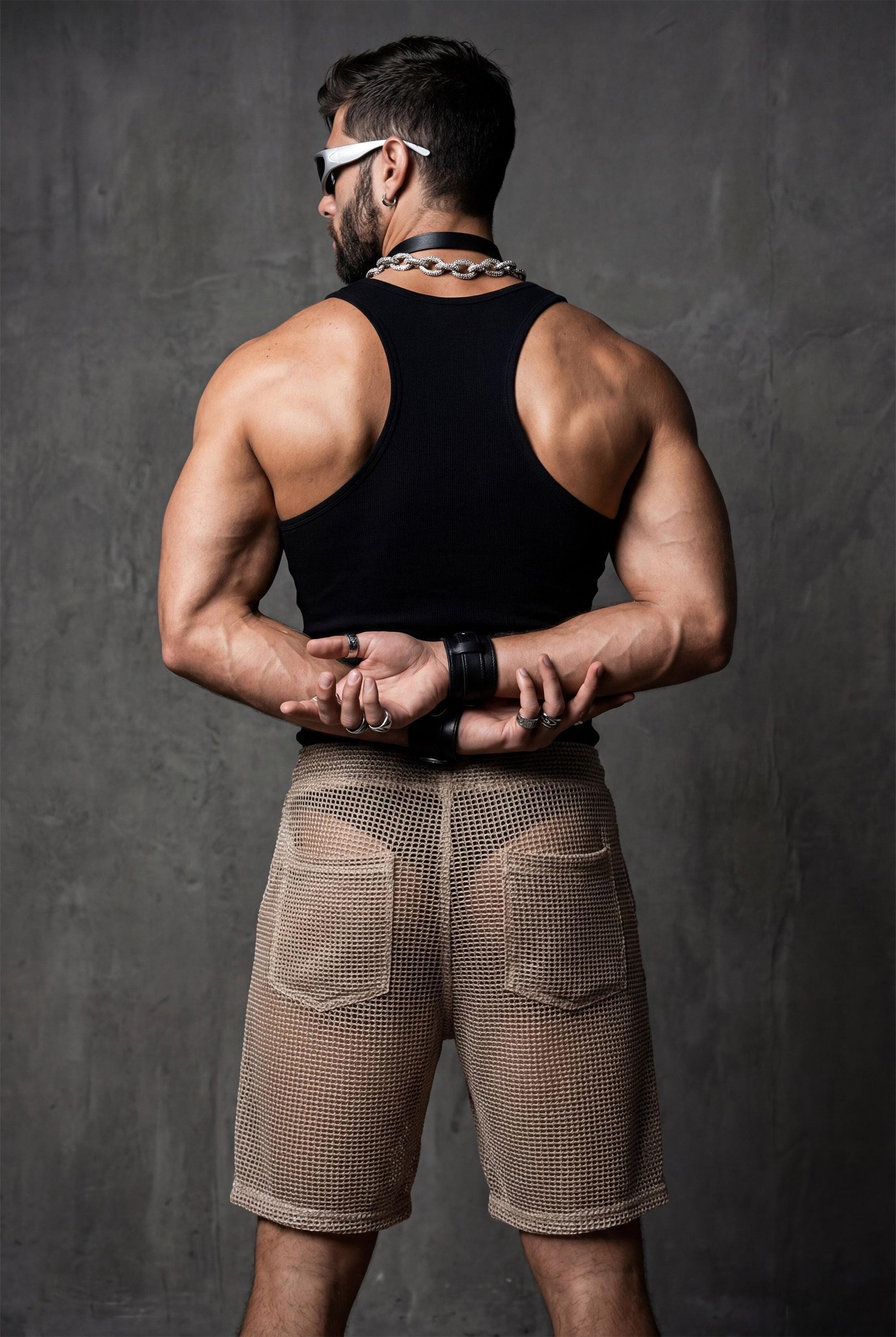 Back view of transparent black mesh shorts on a muscular man. Sheer fabric emphasizes curves and leg definition. Perfect for gay club wear, Berlin party scene, circuit events, and fetish-inspired nightlife. Bold mesh shorts for men seeking sexy, provocative, and breathable party clothing with strong visual impact.