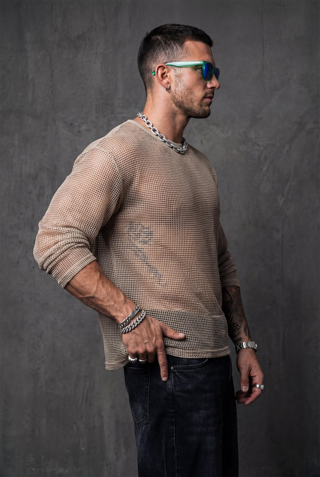 Beige sheer mesh top by PIEL worn from the front by a man. Unisex transparent mesh shirt with fluid straight cut, lightweight breathable fabric revealing the body. Festival wear, clubwear, rave outfit, beachwear, queer fashion, modern minimal unisex clothing.