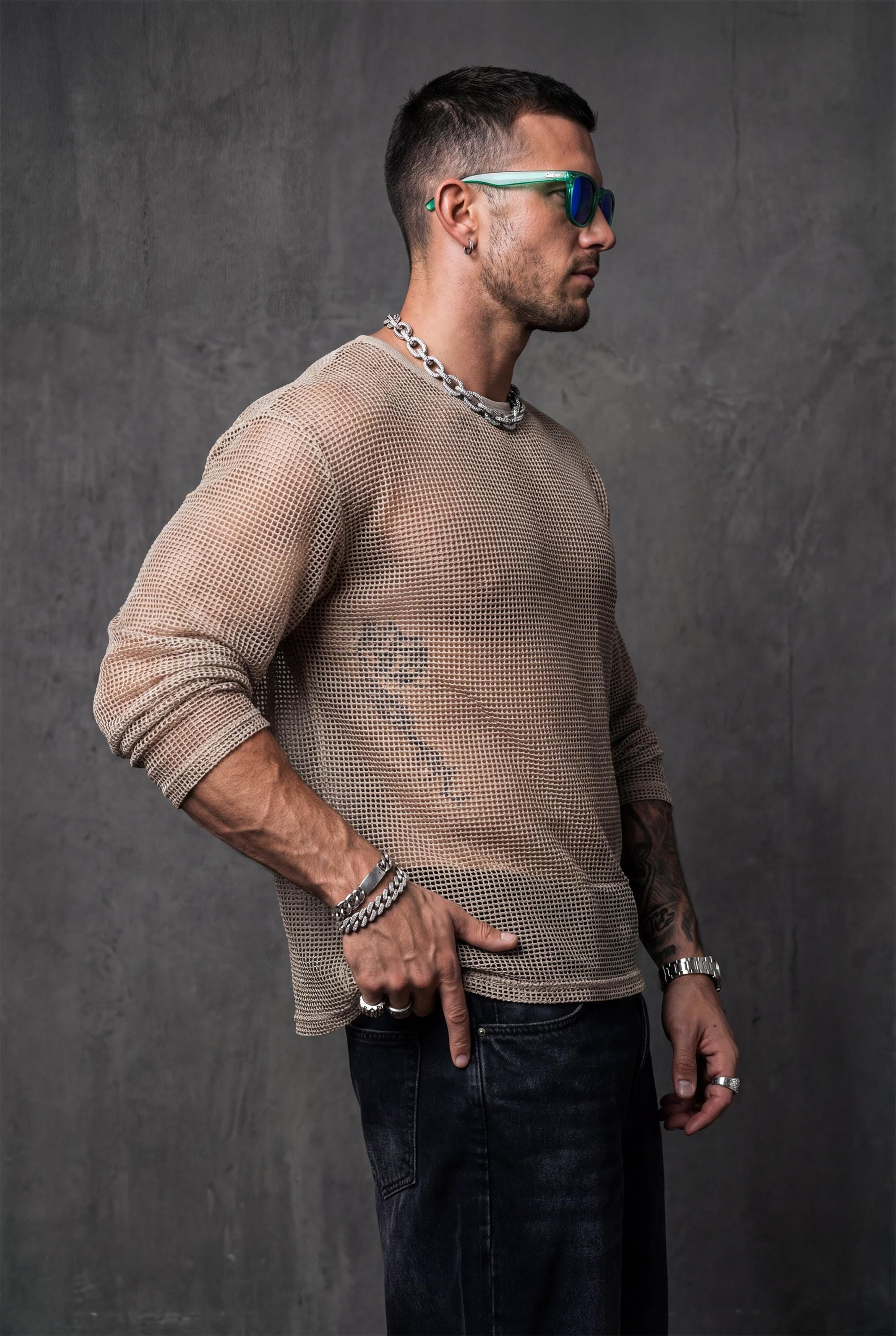 Beige sheer mesh top by PIEL worn from the front by a man. Unisex transparent mesh shirt with fluid straight cut, lightweight breathable fabric revealing the body. Festival wear, clubwear, rave outfit, beachwear, queer fashion, modern minimal unisex clothing.