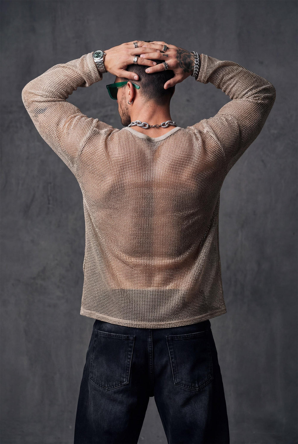 Back view of beige sheer mesh top by PIEL worn by a man. Unisex transparent mesh shirt with straight fluid cut, lightweight breathable fabric revealing the back. Festival wear, clubwear, rave outfit, beachwear, queer fashion, modern minimalist unisex clothing.