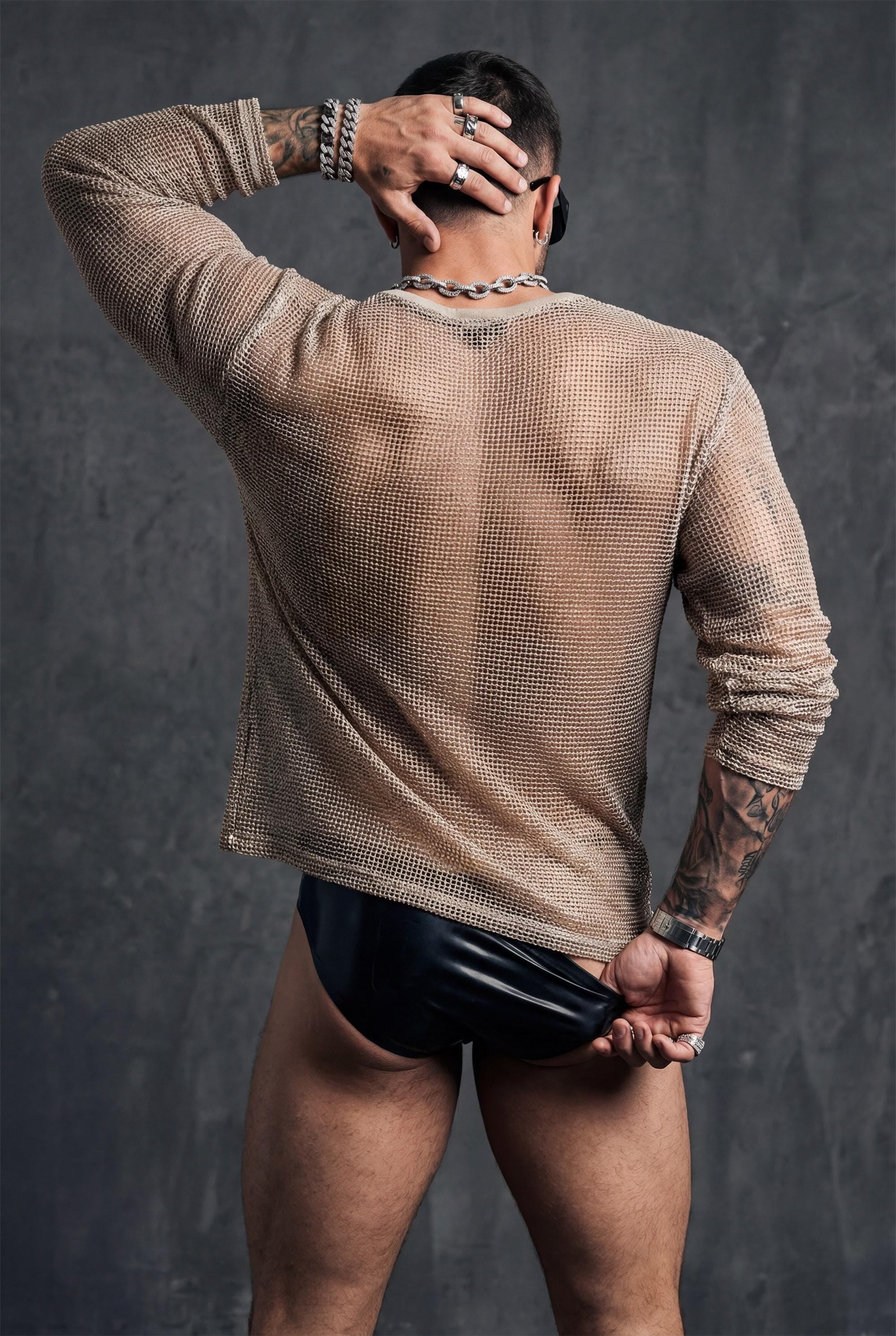 Back view of beige sheer mesh top by PIEL worn by a man. Unisex transparent mesh shirt with straight fluid cut, lightweight breathable fabric revealing the back. Festival wear, clubwear, rave outfit, beachwear, queer fashion, modern minimalist unisex clothing.