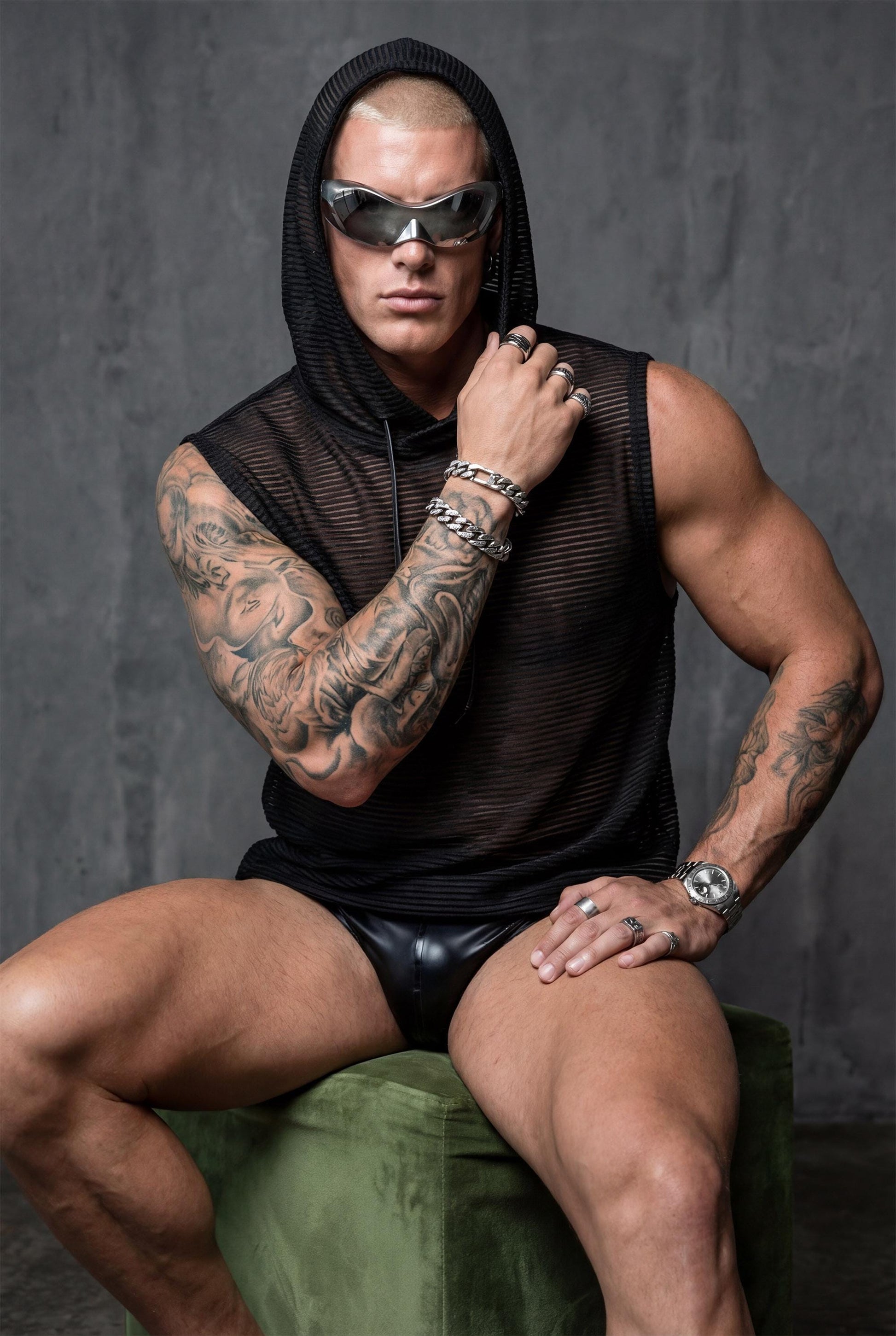 Black mesh hooded tank top men front view showing hood detail and semi-sheer construction with metallic accents. Versatile festival clothing for rave culture enthusiasts, pride parades, and summer adventures. This transparent sleeveless top offers airflow and movement freedom ideal for dancing, performing, or beachside confidence. Bold queer fashion combining urban edge with breathable comfort for nightlife