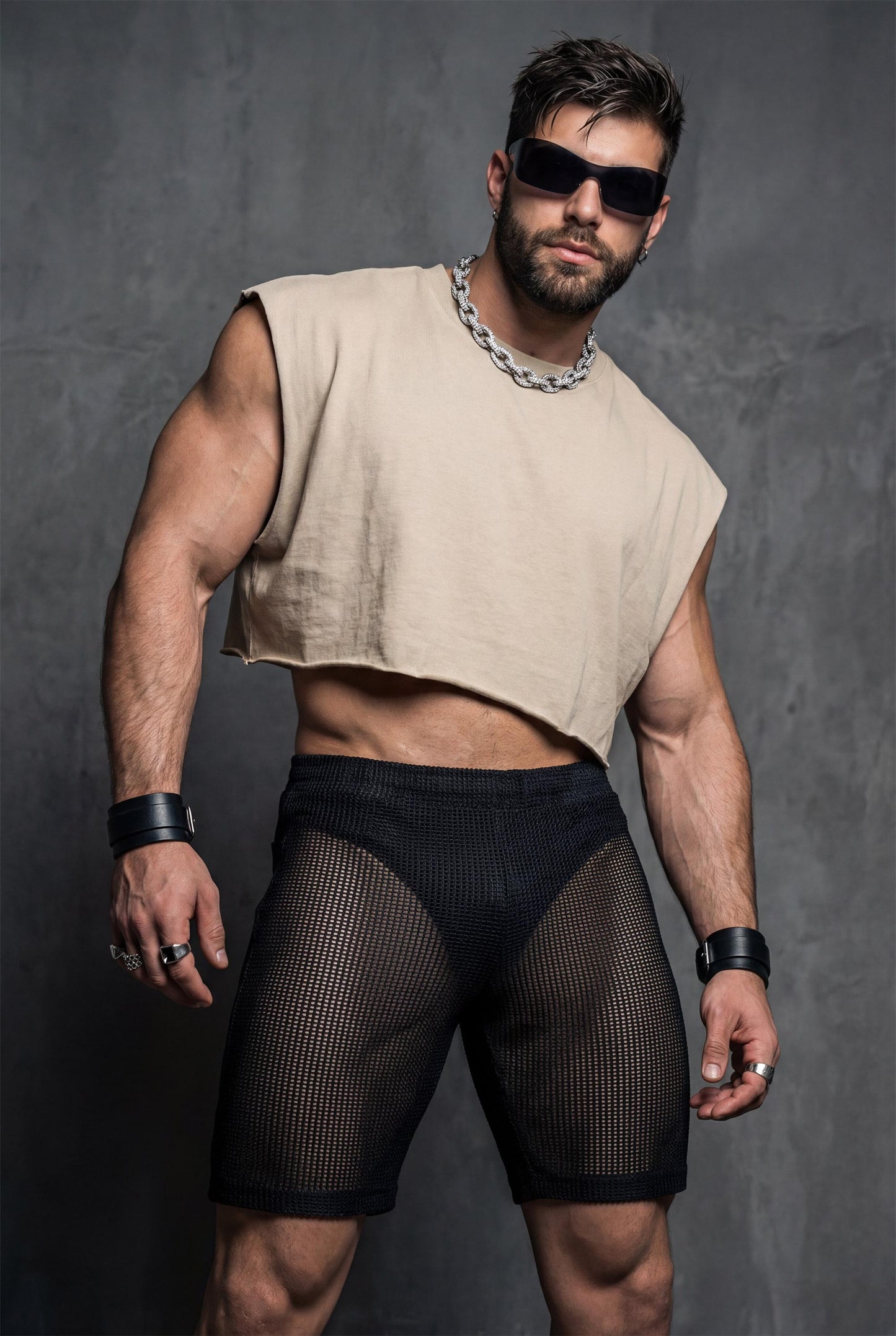 Front view of black transparent mesh shorts worn by a muscular man. Sheer fabric reveals the body underneath while keeping a fitted, athletic cut. Designed for gay club wear, Berlin nightlife, circuit parties, and pride events. Sexy, breathable party shorts for men who want bold, confident, and eye-catching club outfits.