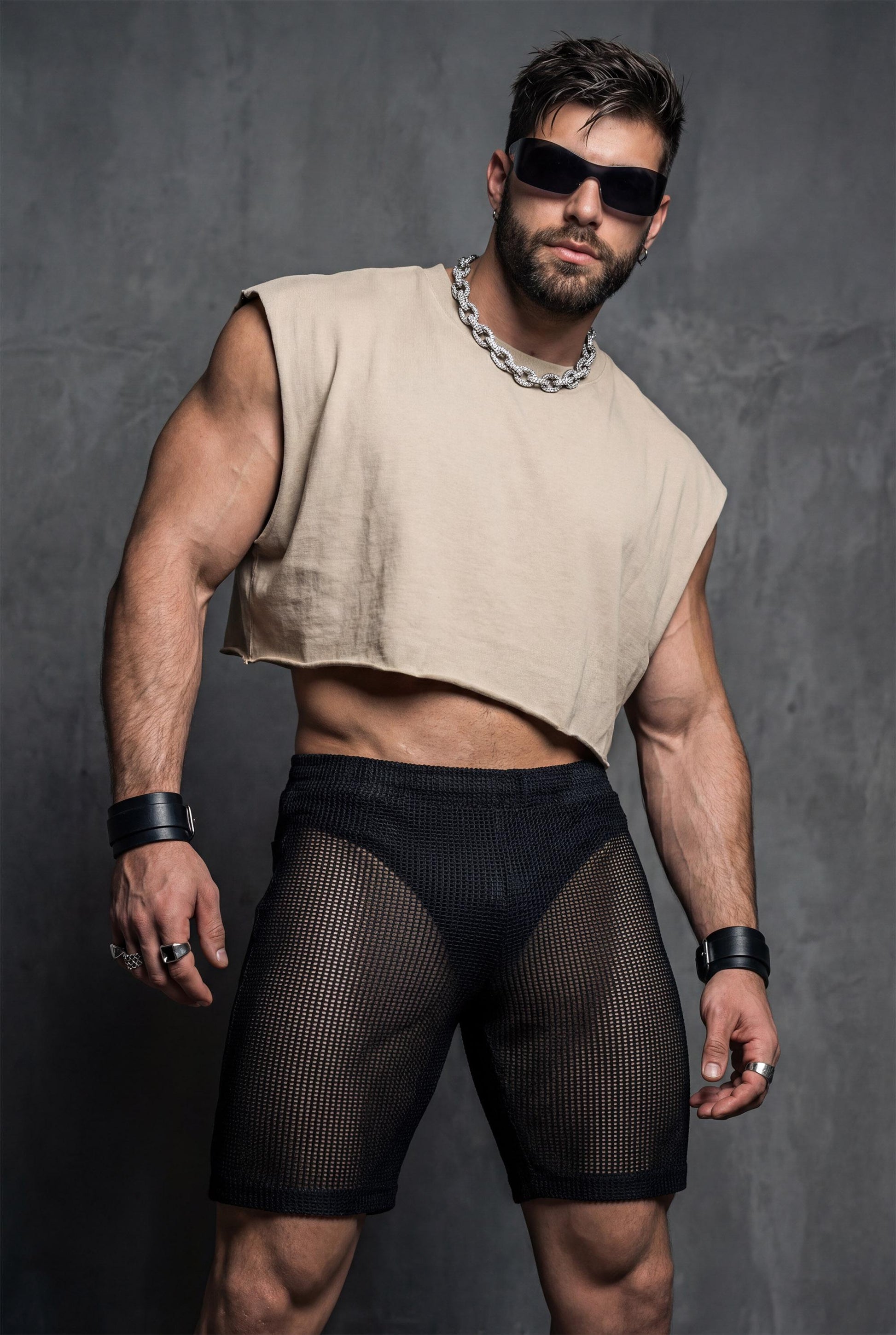 Front view of black transparent mesh shorts worn by a muscular man. Sheer fabric reveals the body underneath while keeping a fitted, athletic cut. Designed for gay club wear, Berlin nightlife, circuit parties, and pride events. Sexy, breathable party shorts for men who want bold, confident, and eye-catching club outfits.