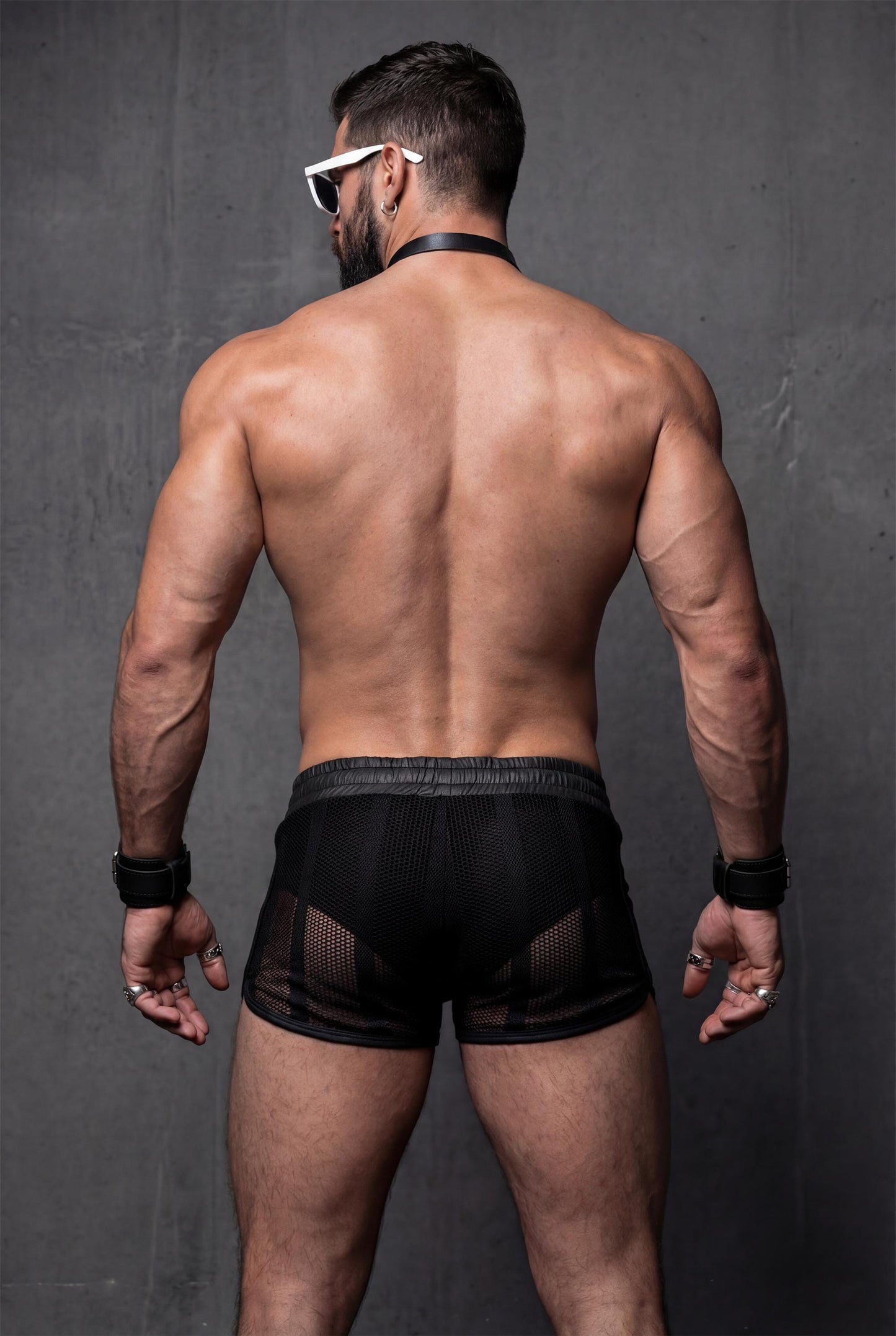 Back view of black mesh shorts for men with sheer see-through construction. Transparent festival shorts highlighting glutes and legs, designed for pride events, circuit parties and bold men’s clubwear looks.