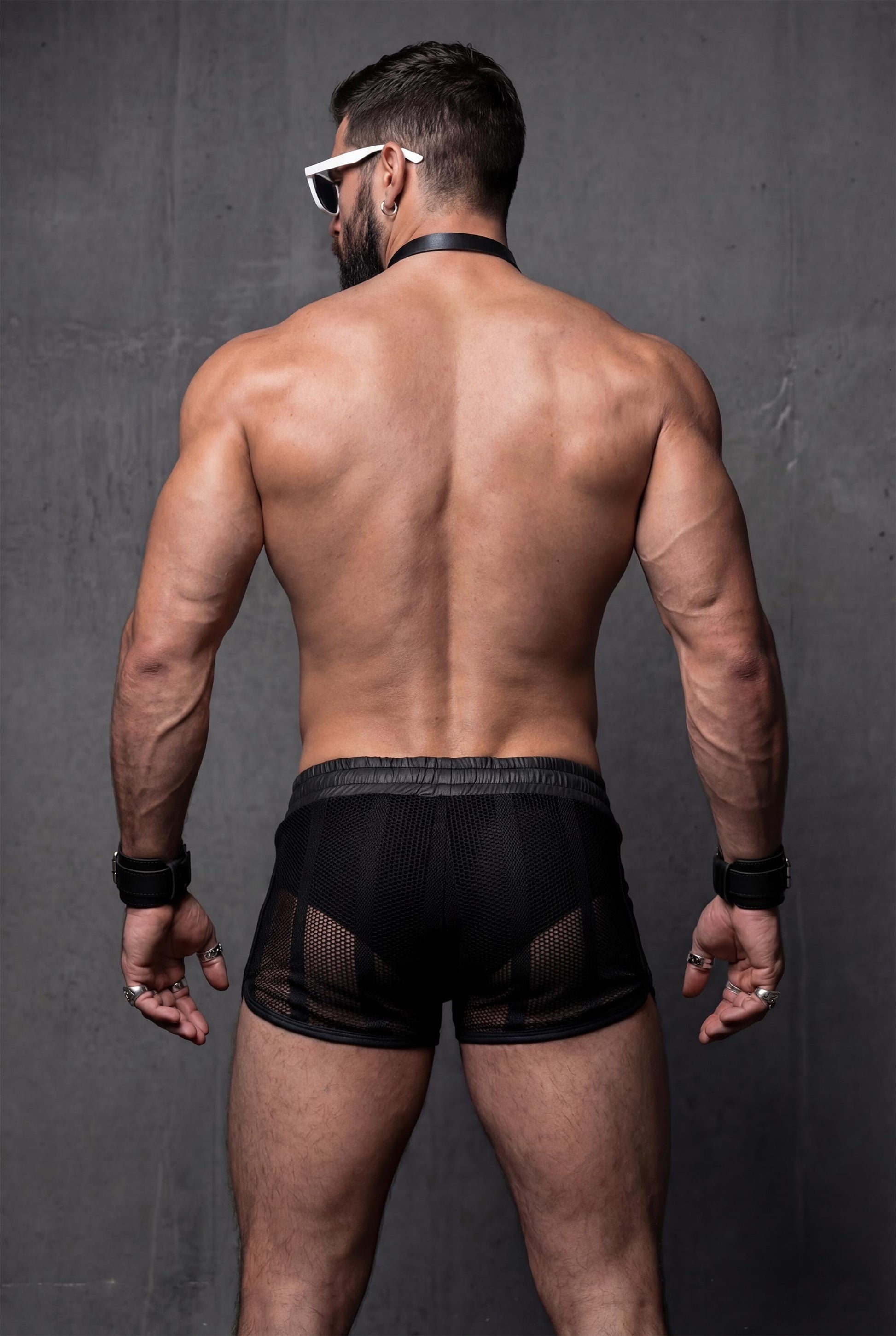 Back view of black mesh shorts for men with sheer see-through construction. Transparent festival shorts highlighting glutes and legs, designed for pride events, circuit parties and bold men’s clubwear looks.