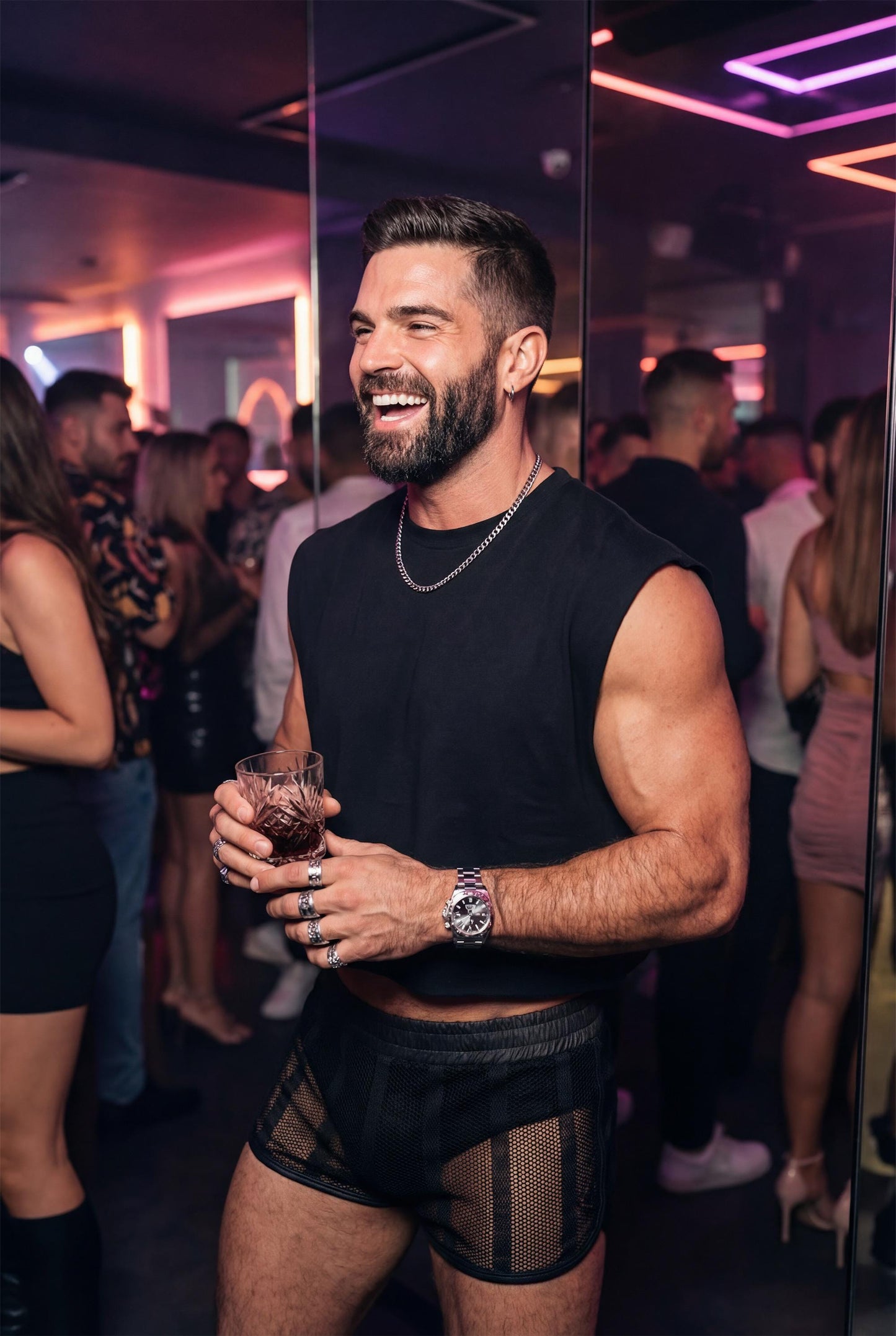Muscular bearded man wearing black sheer mesh shorts and a sleeveless black top, standing in a nightclub with neon lights and a blurred crowd in the background. He holds a drink and smiles confidently, showcasing transparent mesh fabric, athletic legs, and a bold clubwear look. Gay men’s party outfit designed for nightlife, circuit parties, queer events, and club fashion with a strong masculine attitude.