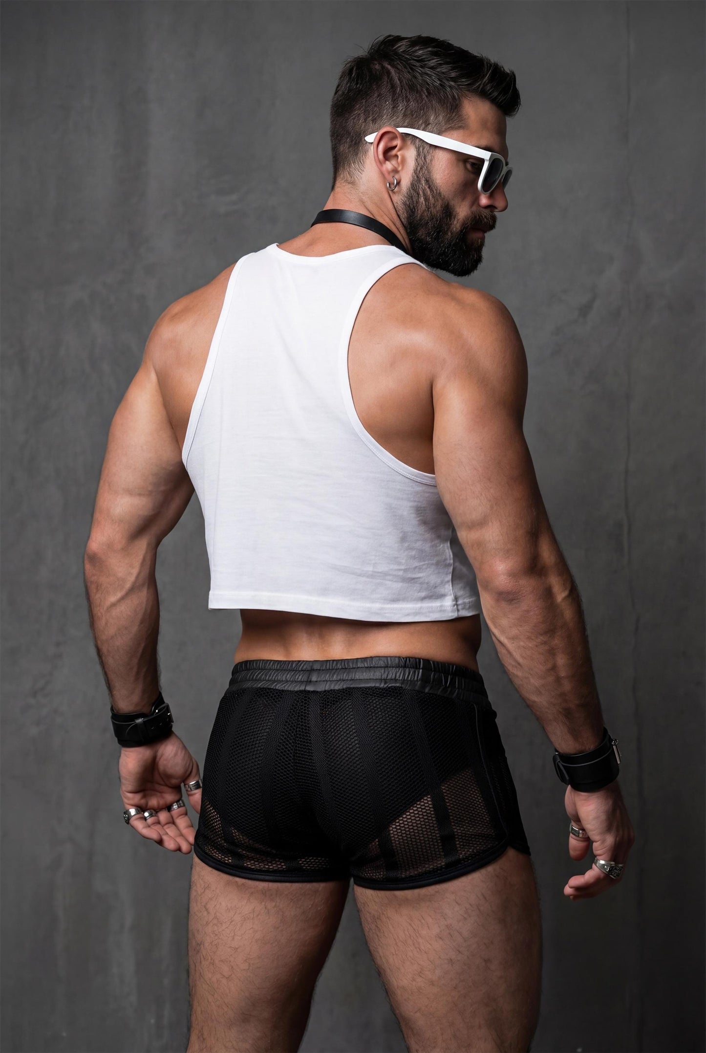 Back view of a muscular man wearing black sheer mesh shorts with see-through fabric and short cut. Transparent men’s festival shorts designed for pride events, circuit parties, club nights and bold gay summer fashion.