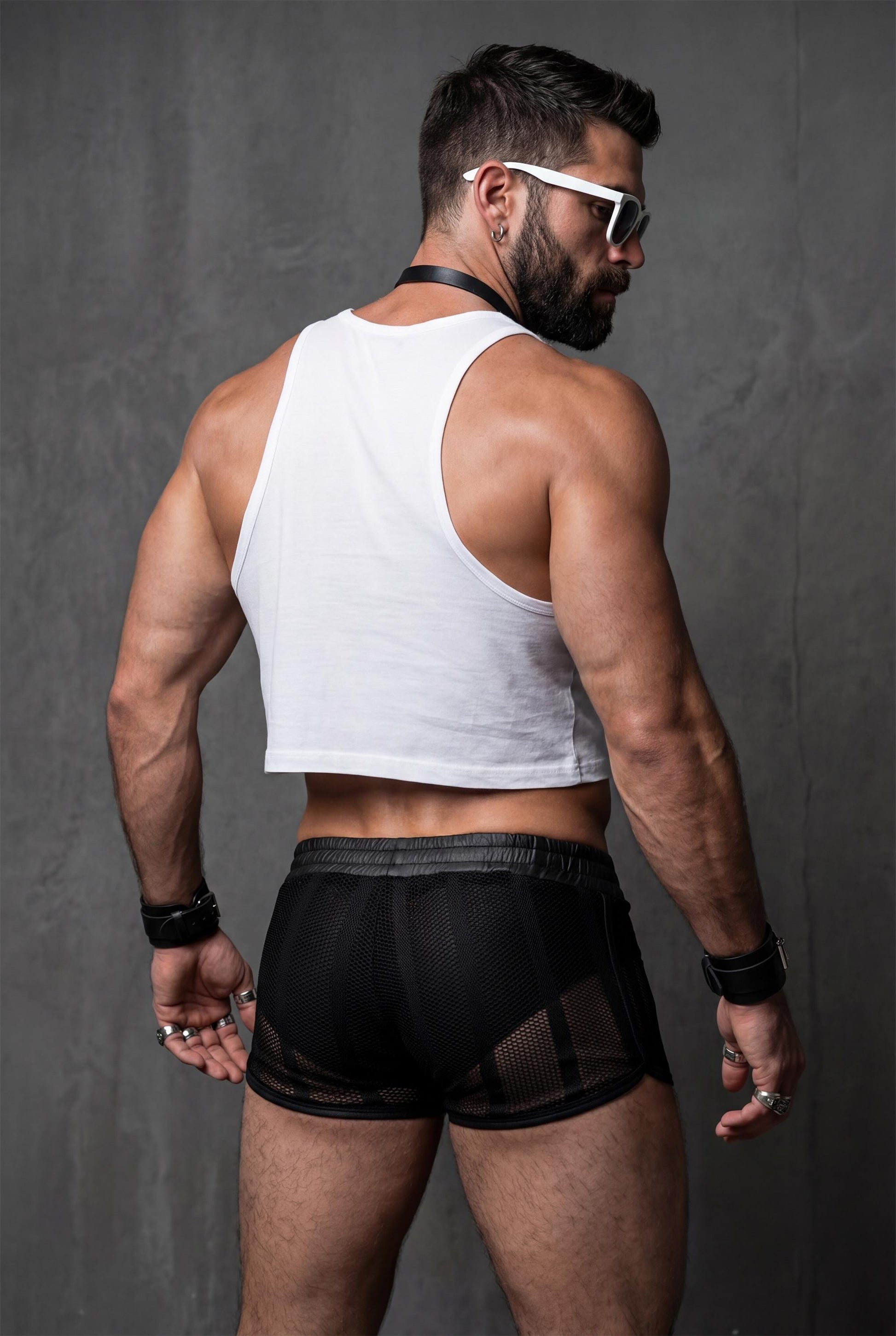 Back view of a muscular man wearing black sheer mesh shorts with see-through fabric and short cut. Transparent men’s festival shorts designed for pride events, circuit parties, club nights and bold gay summer fashion.