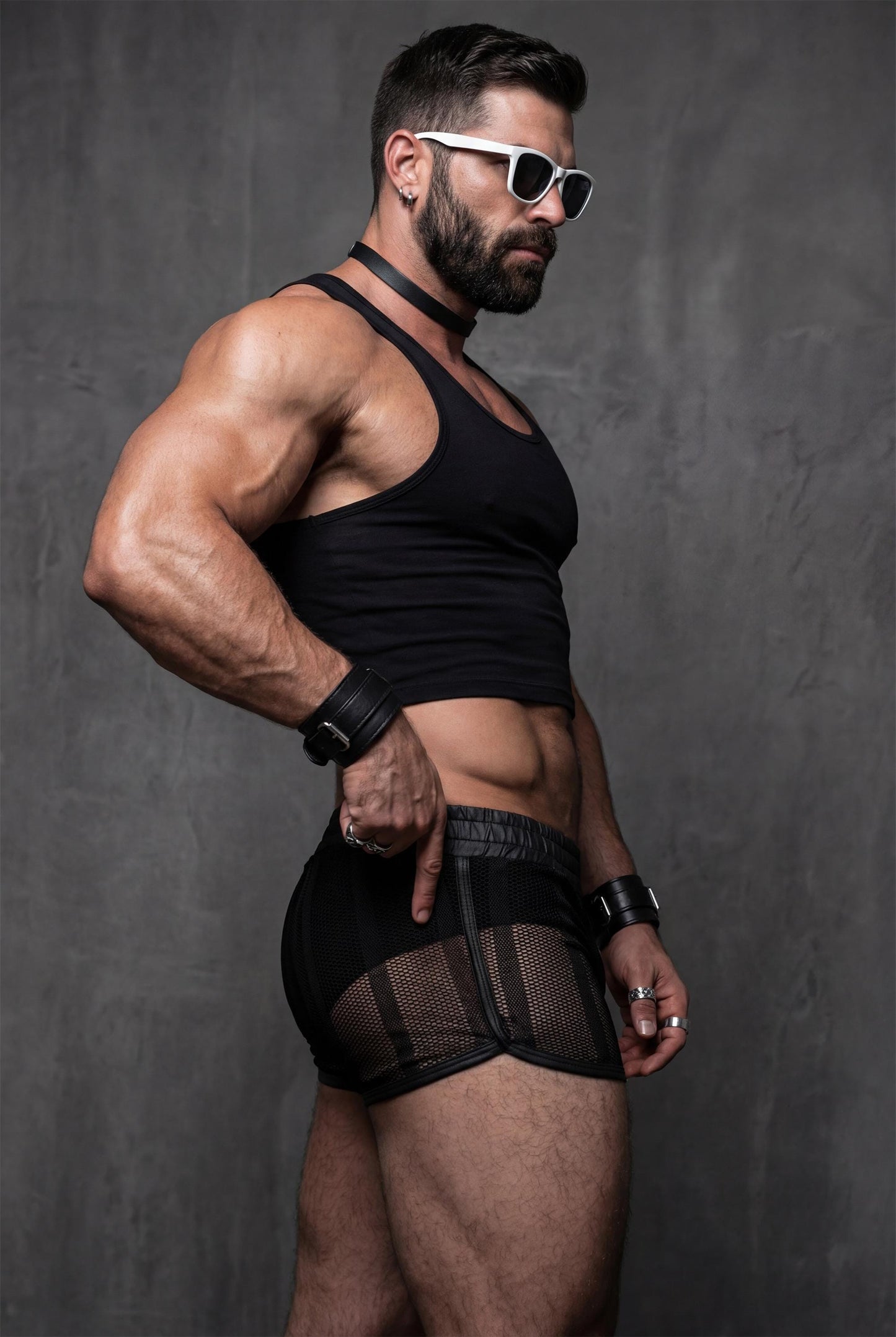 Muscular male model wearing black mesh shorts for men with sheer see-through fabric and snug short cut. Transparent festival shorts revealing body contours, designed for pride events, circuit parties and men’s gay clubwear with breathable quick-dry mesh.