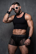 Muscular male model wearing black sheer mesh shorts with fully see-through fabric, snug short cut and faux leather waistband. Transparent men’s festival shorts revealing body shape, styled with crop top for pride events, circuit parties, club nights and bold gay clubwear looks.