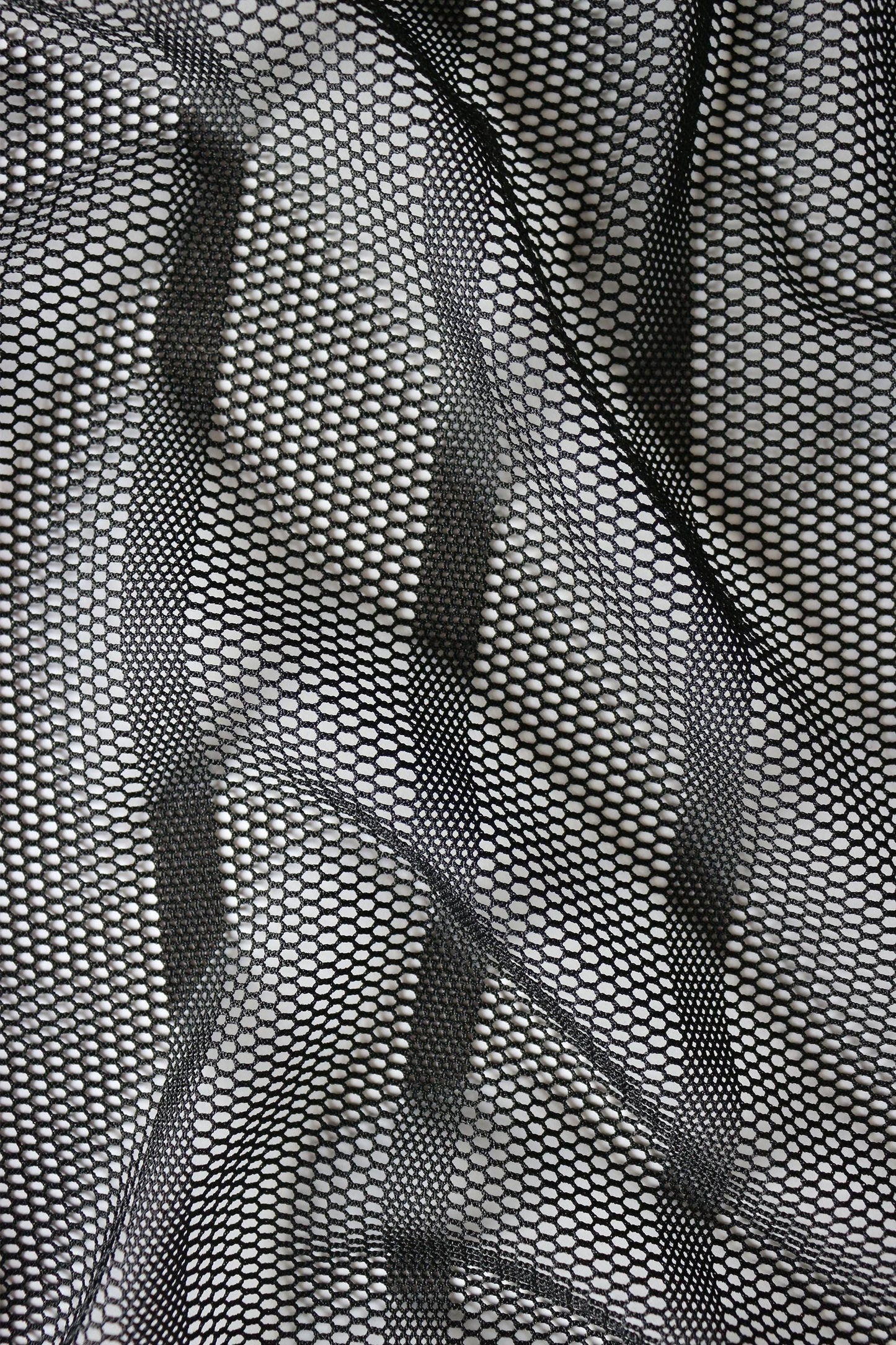 Close-up detail of black sheer mesh fabric showing vertical stripe texture and see-through construction for tank top. Breathable open-weave pattern creates transparent look perfect for rave wear and gay festival fashion. Durable lightweight material maintains shape. Ideal for circuit parties, pride events, and summer style where bold transparent aesthetic matters.