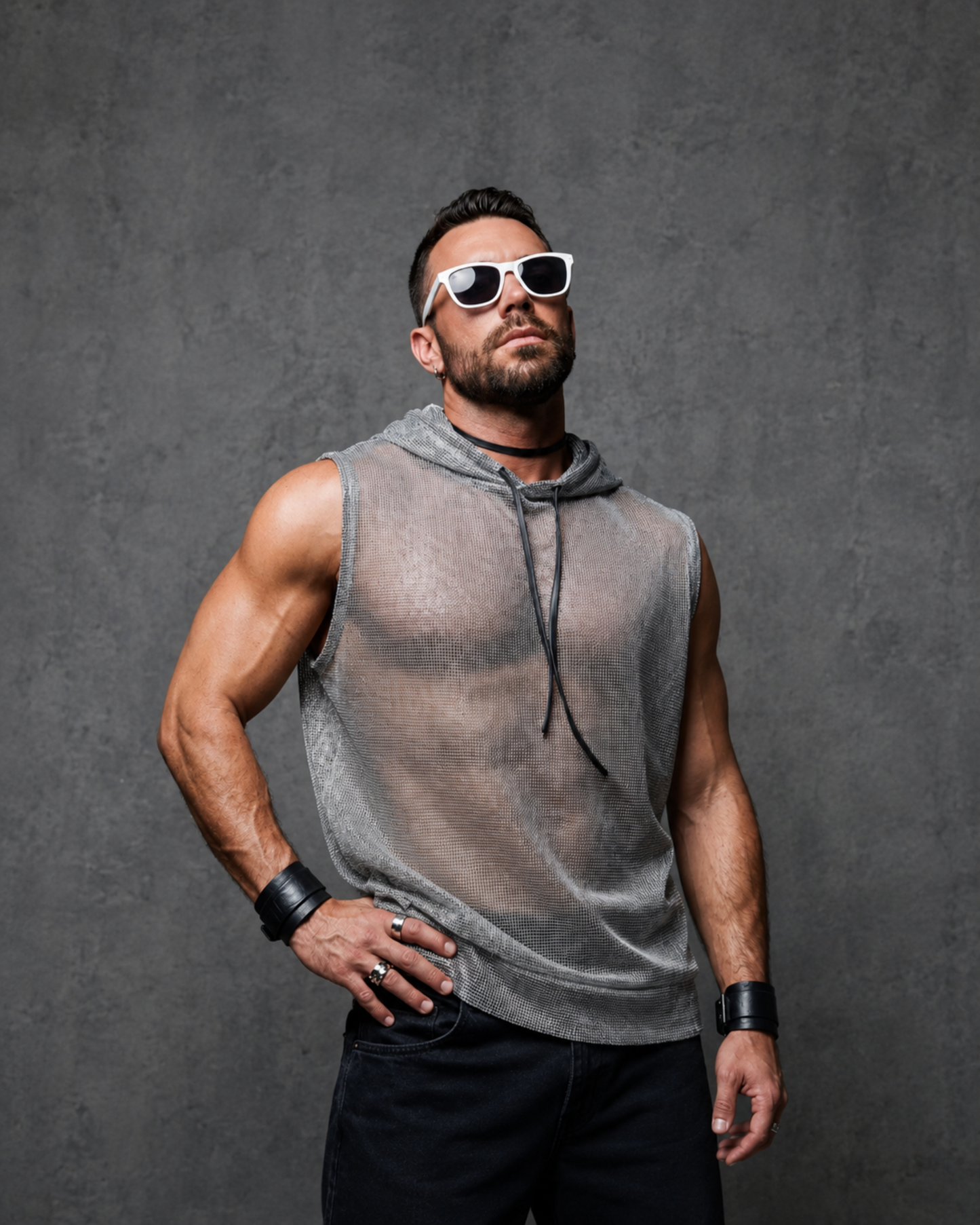 Man wearing a sleeveless hoodie and sunglasses against a gray background