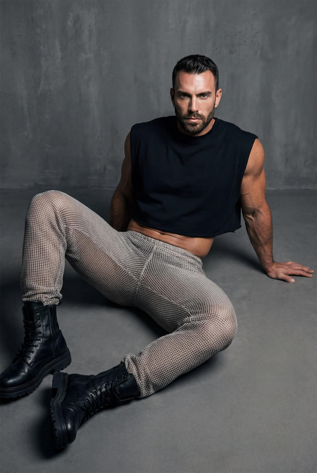 Beige mesh knit jogger pants men side profile showing relaxed leg shape and see-through knit construction for festival outfit and gay casual fashion. Breathable open-weave fabric allows air circulation perfect for dancing in heat. Elastic waistband and cuffs ensure comfortable fit. Ideal for Burning Man style, beach raves, pride events, and outdoor parties. Versatile joggers transition from daytime lounging to nighttime festivities. Statement piece for men building wardrobe with confidence.