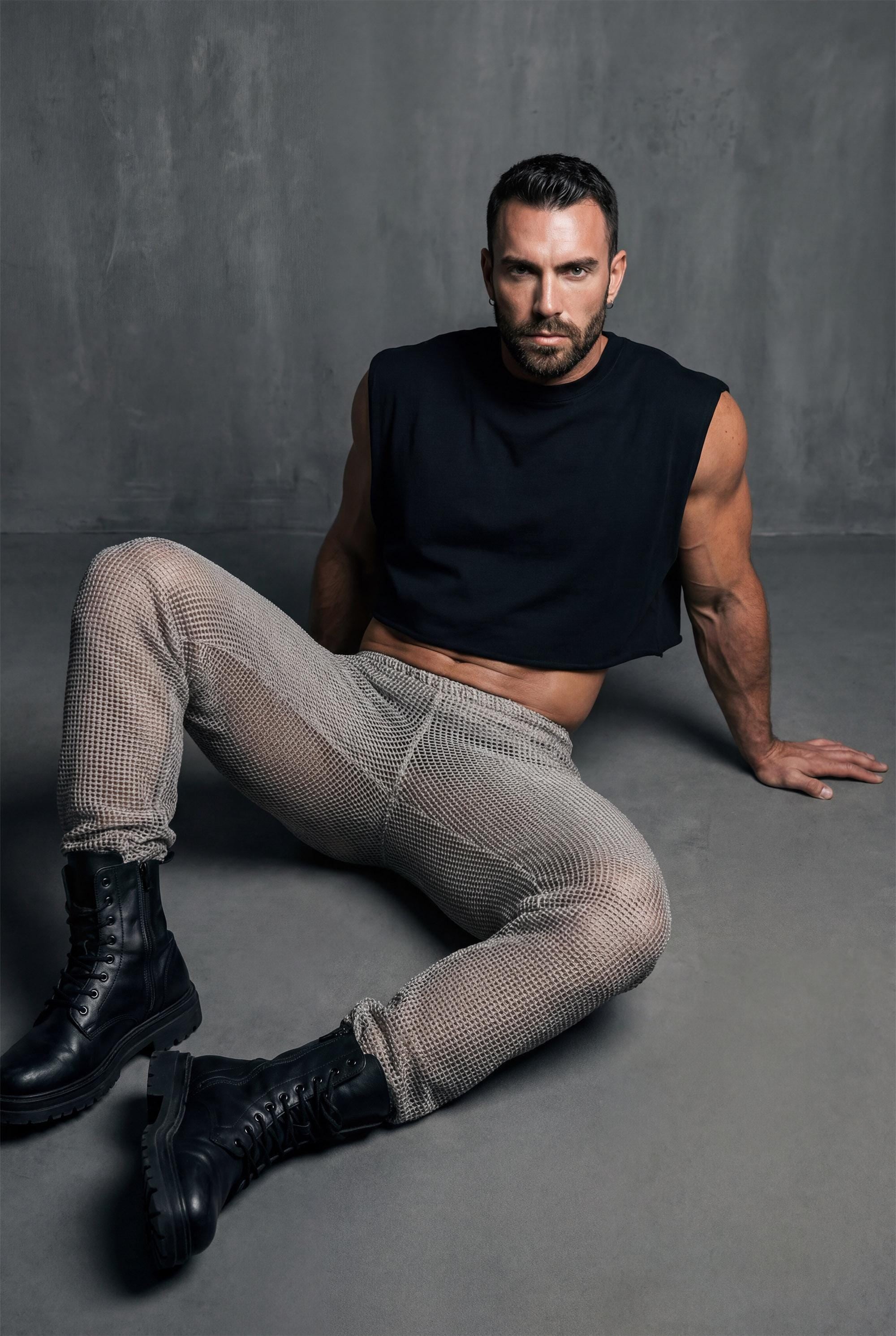 Beige mesh knit jogger pants men side profile showing relaxed leg shape and see-through knit construction for festival outfit and gay casual fashion. Breathable open-weave fabric allows air circulation perfect for dancing in heat. Elastic waistband and cuffs ensure comfortable fit. Ideal for Burning Man style, beach raves, pride events, and outdoor parties. Versatile joggers transition from daytime lounging to nighttime festivities. Statement piece for men building wardrobe with confidence.