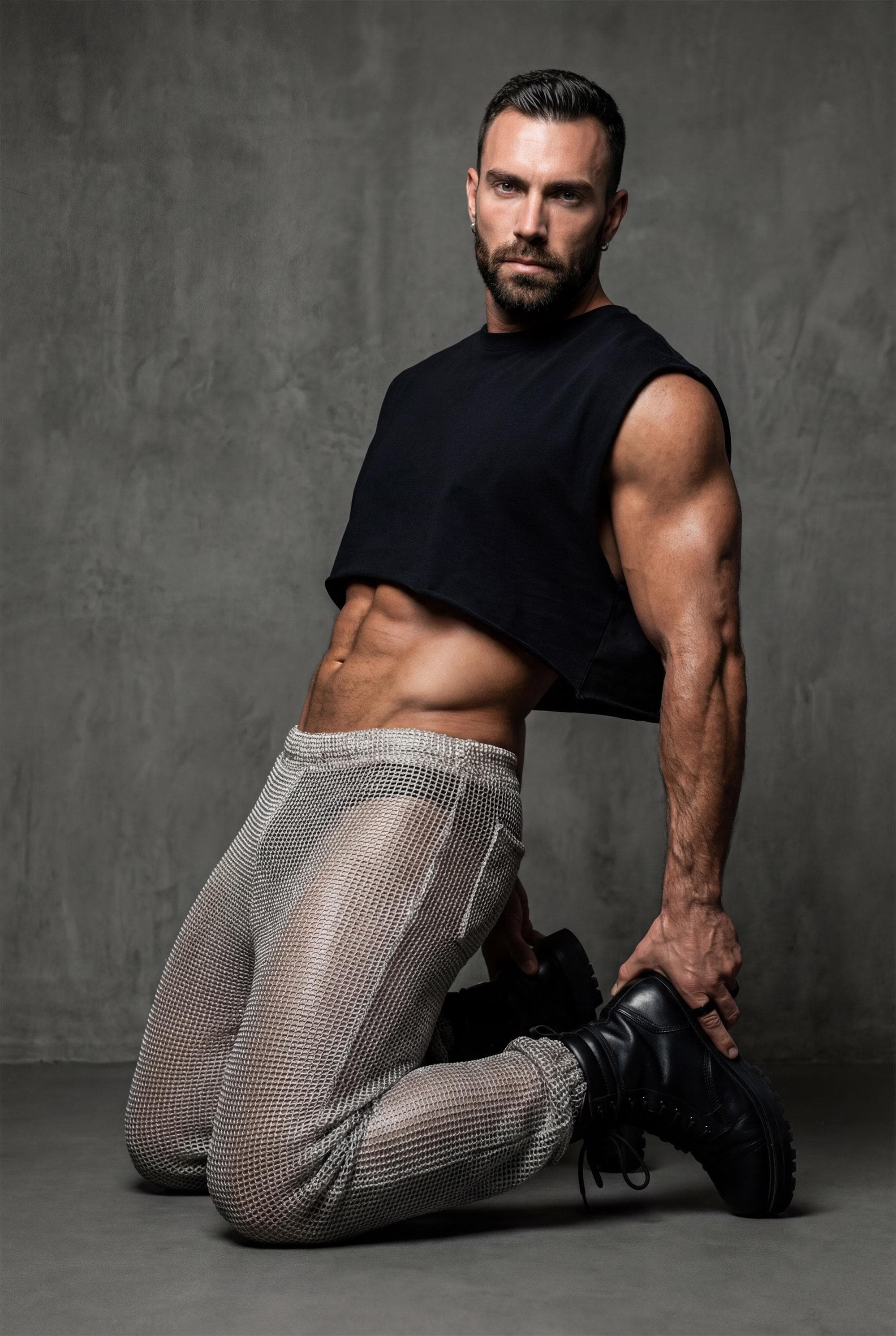 Beige mesh knit jogger pants men side profile showing relaxed leg shape and see-through knit construction for festival outfit and gay casual fashion. Breathable open-weave fabric allows air circulation perfect for dancing in heat. Elastic waistband and cuffs ensure comfortable fit. Ideal for Burning Man style, beach raves, pride events, and outdoor parties. Versatile joggers transition from daytime lounging to nighttime festivities. Statement piece for men building wardrobe with confidence.