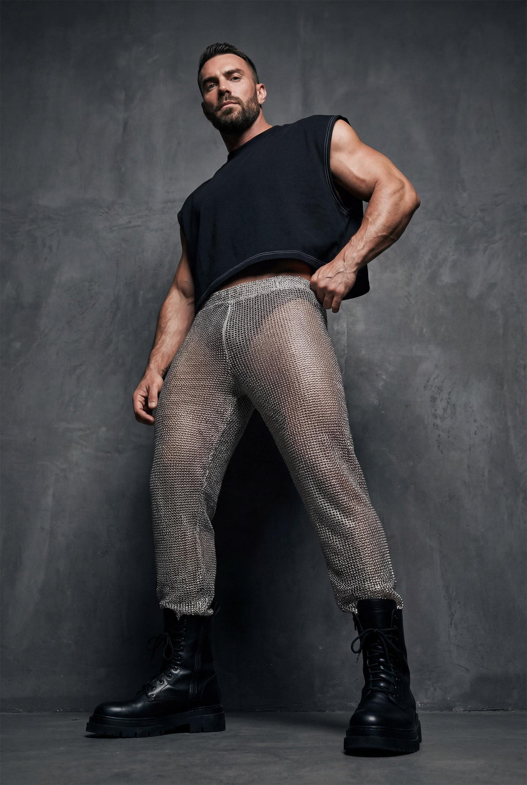 Beige mesh knit jogger pants men side profile showing relaxed leg shape and see-through knit construction for festival outfit and gay casual fashion. Breathable open-weave fabric allows air circulation perfect for dancing in heat. Elastic waistband and cuffs ensure comfortable fit. Ideal for Burning Man style, beach raves, pride events, and outdoor parties. Versatile joggers transition from daytime lounging to nighttime festivities. Statement piece for men building wardrobe with confidence.