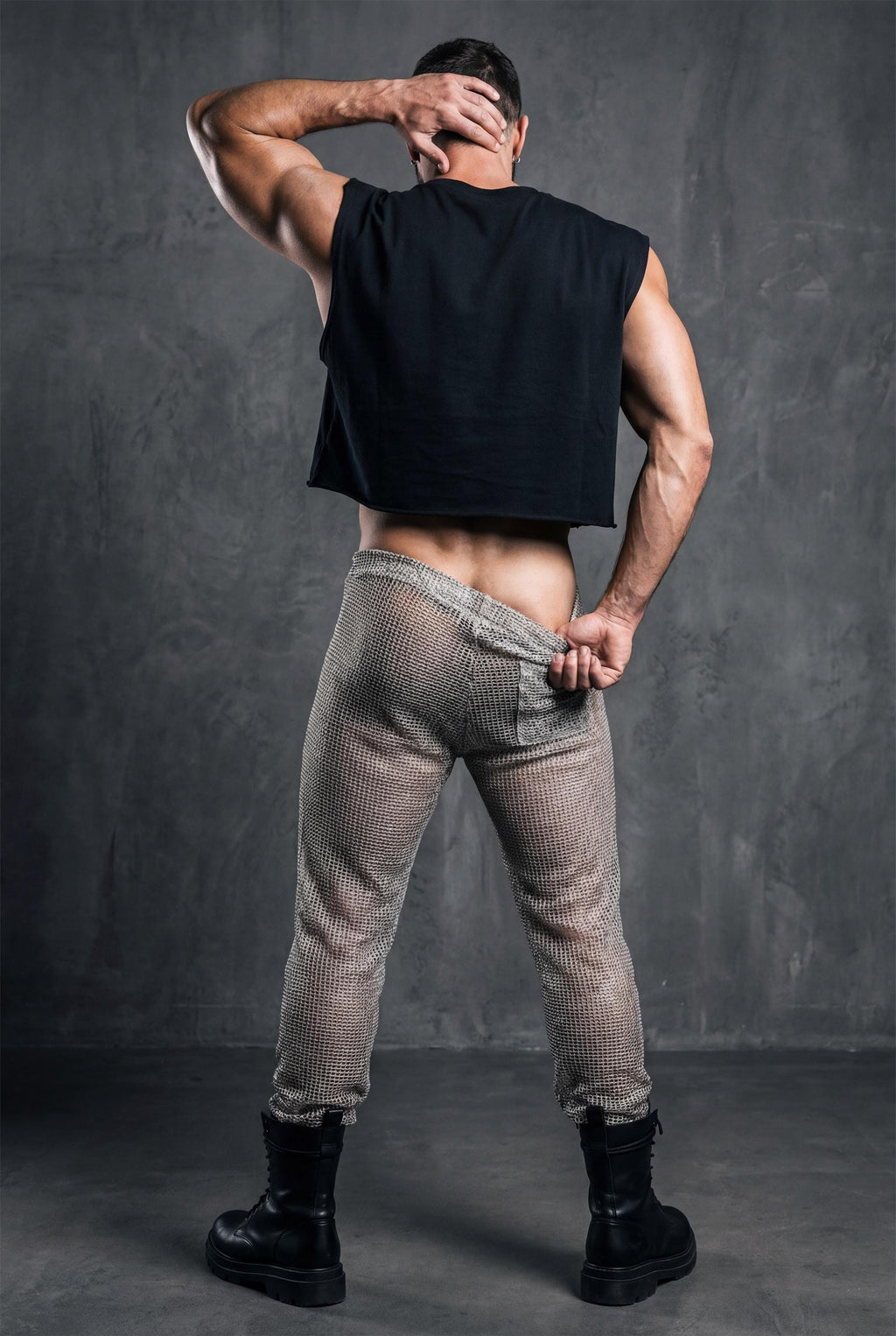 Beige see-through knit mesh jogger pants. Open-knit texture creates breathable airy feel while revealing skin beneath. Ideal for Burning Man, beach parties, pride festivals, and circuit party style. Shows versatility of matching separates. Essential coordinated look for men embracing bold transparent aesthetic with confident self-expression and unique festival fashion sense.