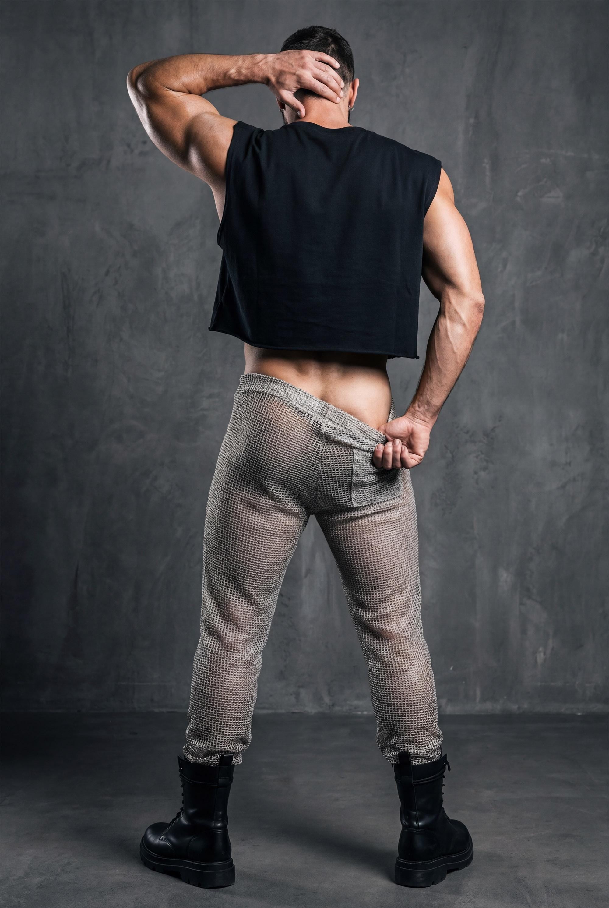 Beige see-through knit mesh jogger pants. Open-knit texture creates breathable airy feel while revealing skin beneath. Ideal for Burning Man, beach parties, pride festivals, and circuit party style. Shows versatility of matching separates. Essential coordinated look for men embracing bold transparent aesthetic with confident self-expression and unique festival fashion sense.