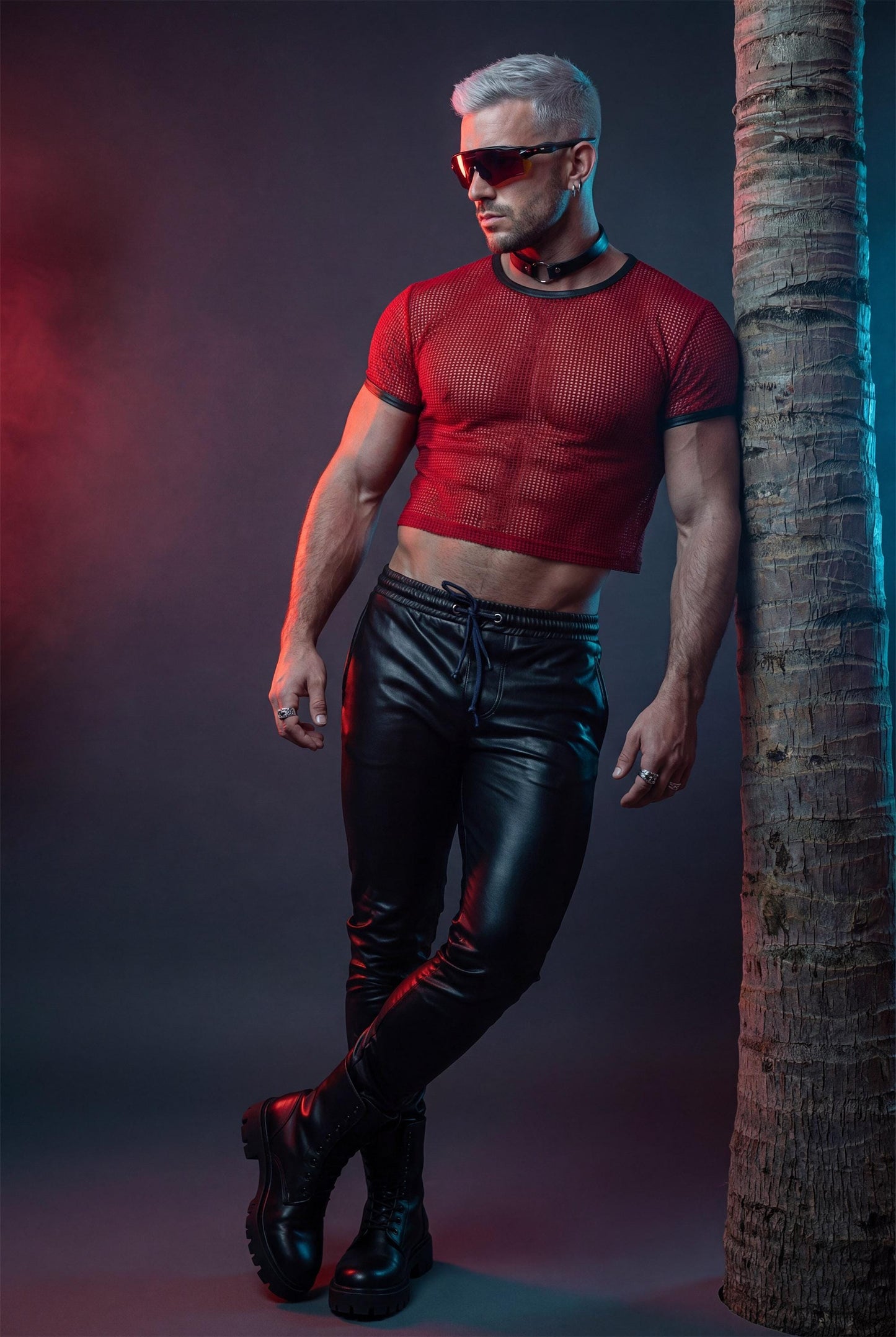 Muscular man wearing a red PIEL men’s mesh crop top in a studio setting. The short mesh top features an open net fabric, fitted cut, and cropped length that highlights the chest, abs, and arms. Men’s mesh crop top designed for clubwear, party outfits, summer looks, and bold masculine fashion. PIEL mesh top with confident, modern style.